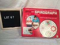 Red cardboard box with colorful graphics showing boys drawing with the Spirograph, various spirograph patterns displayed, and brand name Kenner Spirograph.