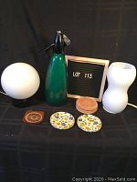 Photo showing two lights, green seltzer bottle, cork coasters, metal floral coasters, and one enamel coaster.