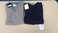 Two folded men's sweaters, one grey and one dark navy, laid side-by-side on a white surface.