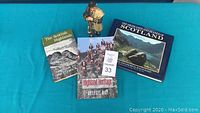 Three books about Scotland and a Royal Doulton figurine of a Scottish laird playing bagpipes, set on a blue surface.