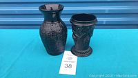 Two antique black amethyst glass vases side by side on a blue surface.