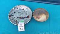 Photo showing circular wall plaque and lightweight bowl laid on blue surface with auction lot number visible