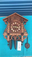 Front view of carved wooden cuckoo clock showing chalet-style case, dial and pinecone weights