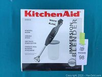 Front of original KitchenAid box showing white immersion blender with stainless steel blending attachment and key product features.
