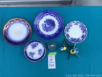 Photo showing four antique flow blue china plates and two bird figurines on a blue surface for the lot containing 12 assorted pieces.