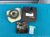 Full view of all three items: bronze coiled dragon candle holder on box, pottery chamber stick candle holder, and decorative mosaic plate.