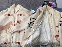 Two vintage cream-colored cable knit sweaters, one with a horse pattern and zipper, the other with button closure and embroidered animal on sleeve, both lined.