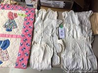 Overview of the crib quilt with appliquéd child figures and several vintage white cotton children's tops folded beside it.