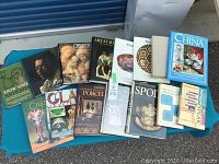 Full lot of 15 antique and collectible reference books shown spread out on a blue cloth, includes books on antiques, glass, porcelain, and decorative arts.
