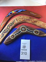 Three wooden boomerangs arranged next to auction tag 310, showing painted Aboriginal style designs and 'Australia' markings.