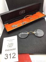 Photo showing two pairs of vintage spectacles, one pince-nez style with gold-tone metal frame and one in a black case with orange interior lining.