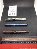 Three vintage fountain pens laid flat with ruler for scale showing lengths approximately 5 inches. Pens identified as Parker (brown), Waterman (grey), and Esterbrook (blue).