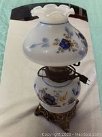 Full view of vintage electric table lamp showing floral milk glass shade and base with connected power cord and decorative metal base.