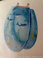 Photo of dolphin-themed toilet seat showing the lid with three dolphin figures and underwater plants design.