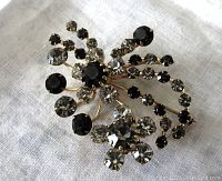 Front view of vintage floral brooch with clear and black glass stones in multi-prong settings on gold-tone backing.