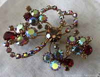Front view of vintage brooch showing champagne center stone, red teardrop rhinestones, and aurora borealis rhinestones in brass setting.
