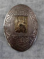 Front view of oval pendant/brooch showing pressed geometric and symbolic design in sterling silver with central applied 18K yellow gold piece with raised Inca style motif.