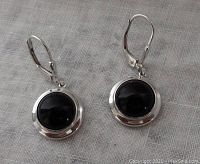Front view of the pair of black onyx cabochon dangler earrings in sterling silver, lying on fabric.
