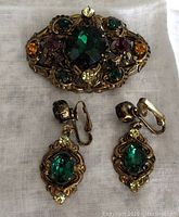 Front view of the brooch and two clip-on earrings showing colorful glass stones in brass settings.