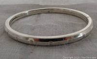 Photo of the closed sterling silver bangle showing its rectangular form and shiny surface with subtle stamping details.