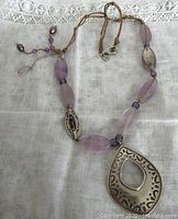 Full view of the necklace laid flat showing the arrangement of oval amethyst beads, silver decorative beads, pendant, and cord.