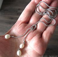 Sterling silver chain necklace with three freshwater pearls dangling, held in palm showing overall length and design.
