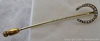 Full length view of the gold stick pin with horseshoe head and seed pearls, showing the gold safety cap and twisted shaft detail.