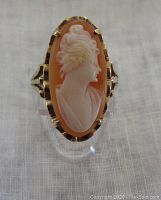Front of the ring showing the marquise-shaped shell cameo with a carved female profile in cream color against an orange background in a yellow gold setting.
