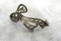 Close-up of antique white gold bow pin showing detailed openwork filigree.