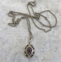 Front view of pendant with amethyst center stone and marcasite stones in silver setting on chain laid flat