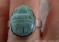 Close-up of turquoise scarab stone on sterling silver ring worn on finger showing carved details.
