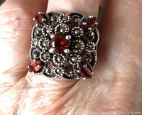Top view of sterling silver ring showing five garnet stones and marcasite accents in ornate openwork design on finger