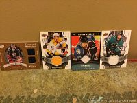 Four NHL game jersey cards upright against a wall on carpet, featuring Paul Kariya, Filip Forsberg, Milan Hejduk, and Marc-Edouard Vlasic.