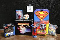Front view of the lunch pail, Superman and Steel action figures, Dorbz Clark Kent figure still in box, and small Superman figure on black background