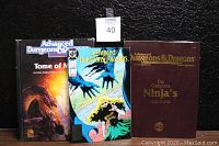 Front view of three Advanced Dungeons & Dragons collectibles including Tome of Magic hardcover, Complete Ninja's Handbook hardcover, and sealed comic book.
