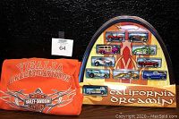 Photo shows the sealed Hot Wheels California Dreamin' 10 vehicle gift set in a shaped collector's case and the orange Harley-Davidson Visalia t-shirt folded beside it.