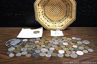 Full view of the woven basket with a spread of many assorted coins laid in front, including a commemorative coin in a card.