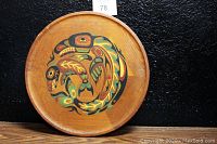 Front view of round wooden shield with colorful Haida-style killer whale design