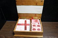 Open hardwood chest displaying vintage floral-themed stationery set including sheets, pencils, and stickers neatly organized inside.