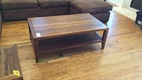 Front view of teak wood coffee table showing rectangular shape, natural wood grain top, square legs, and lower slatted shelf.