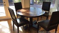 Front and side view of round dining table with copper top and four chairs around it in a sunlit room with wooden floor.