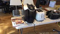 Photo of Keurig coffee maker, Philips toaster, and cookbooks on a table in room with wooden floor