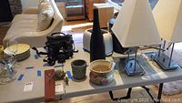 Wide shot showing all three items on a white table: tall black vase, small grey-blue pot, handmade floral pottery piece