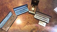 Overview of the Cross Century pen and pencil set, engraved Cross pen, and Pulsar quartz watch in boxes on a table.