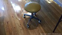 Side and top view of the rolling stool with mustard faux leather round seat on wooden floor
