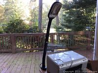 Full lamp standing on deck next to a printer to show scale and clamp base attached to surface edge.