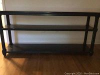 Front angle view of black wooden sofa table with three shelves against wall, showing length and shelf design.