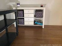 Front view showing white wooden table with four central drawers and fabric storage bins on each side.
