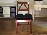 Front view of the wooden chair with black cushion on the seat showing the X-design in the backrest and reddish-brown finish.
