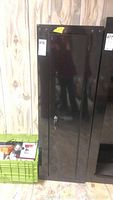 Full view of the black metal storage cabinet showing front door and lock with keys attached.